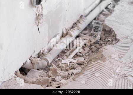Un mur de merde et un tuyau d'évacuation d'eau près du trou dans un sol cassé dans la salle de bains Banque D'Images