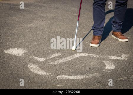 Personne aveugle avec une canne marchant devant un panneau horizontal pour les personnes handicapées peintes sur l'asphalte, concept, problèmes des personnes avec disab Banque D'Images