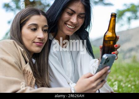 Deux amies qui utilisent un téléphone portable tout en socialisant dans un cadre détendu Banque D'Images