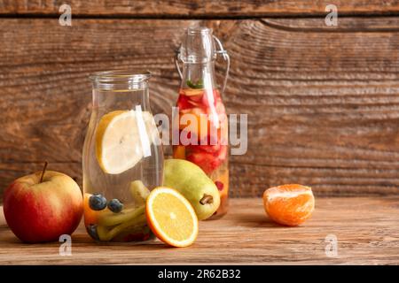 Bouteilles d'eau infusée avec différentes tranches de fruits sur une table en bois Banque D'Images