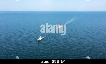 Remorqueur traversant l'océan en tirant une barge jaune chargée de grues de manutention portuaires à chenilles. Vue avant de l'antenne large. Banque D'Images