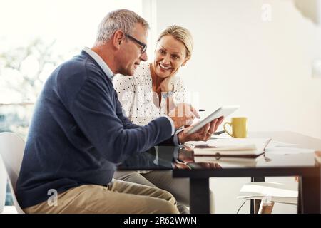 Mettre la technologie au service de leur processus budgétaire. un couple mature utilisant une tablette numérique tout en passant par la paperasse à la maison. Banque D'Images