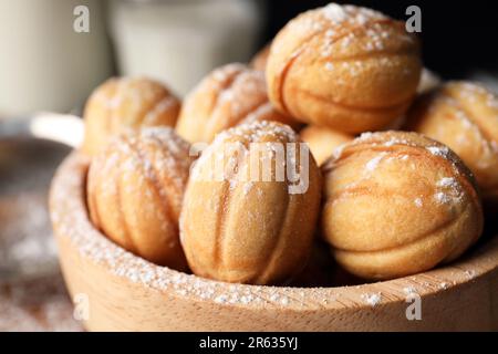 Délicieux biscuits en forme de noix avec sucre en poudre dans un bol en bois, gros plan Banque D'Images