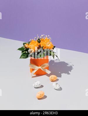 Boîte cadeau orange avec fleurs printanières et œufs de Pâques sur la table. Arrière-plan violet. Composition de Pâques. Minimalisme. Banque D'Images