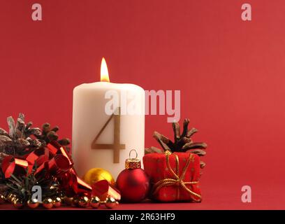 Quatrième bougie de l'Avent brûle, bougie blanche avec le numéro quatre sur fond rouge, décoration de Noël, espace pour le texte Banque D'Images