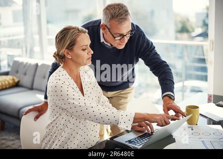 Calcul de leurs dépenses en couple. un couple d'âge mûr utilisant un ordinateur portable tout en passant par la paperasse à la maison. Banque D'Images