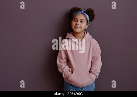 Mini portrait de la taille vers le haut de mignonne fille noire souriant à l'appareil photo portant un sweat à capuche rose, espace de copie Banque D'Images