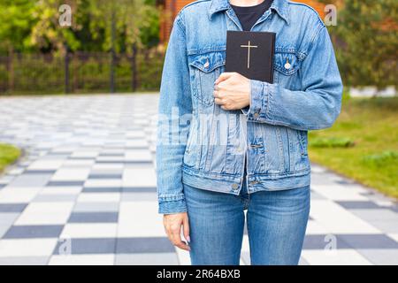 femme tenant une bible dans sa main debout près de l'église. homme tenant la bible. bible avec une croix sur la couverture. Photo de haute qualité Banque D'Images