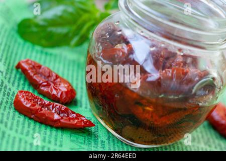 Tomates séchées au soleil avec basilic, ail, romarin et épices dans un pot en verre sur une serviette verte. Banque D'Images