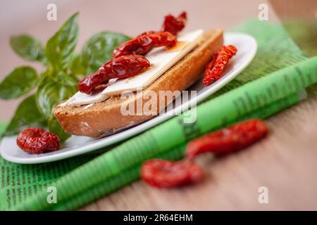 Bruschetta à l'huile d'olive, tomates séchées, feta et basilic frais sur une assiette blanche, serviette verte, table en bois. Banque D'Images