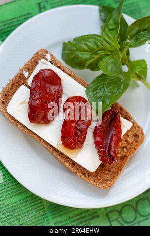 Bruschetta à l'huile d'olive, tomates séchées, feta et basilic frais sur une assiette blanche, serviette verte, table en bois. Banque D'Images