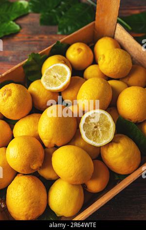 Boîte de citrons jaunes mûrs avec feuilles de citronniers fraîches Banque D'Images