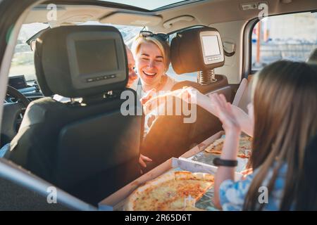 Portrait d'une jeune femme en train de rire avec une pizza italienne pendant qu'elle voyage avec sa famille dans une voiture moderne. Des moments de famille heureux et des valeurs, la restauration rapide Banque D'Images