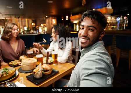 Joyeux groupe multiracial de jeunes amis dans des vêtements décontractés manger au restaurant Banque D'Images