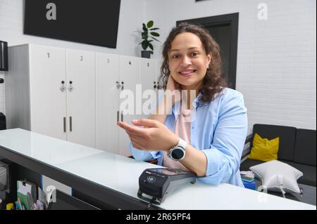 Femme souriante multi-ethnique, cliente, cliente qui paie par montre-bracelet intelligente à l'aide de la technologie NFC. Banque D'Images