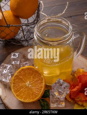 Un verre contient du jus d'orange avec de la glace, avec un panier d'oranges à côté Banque D'Images