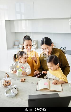 Image verticale d'amis heureux jouant et lisant le livre aux enfants tout en étant assis ensemble dans la cuisine Banque D'Images