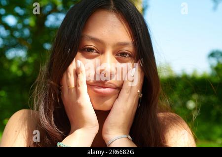 Portrait d'une belle fille asiatique de race mixte assise à l'extérieur dans le jardin au soleil de printemps Banque D'Images