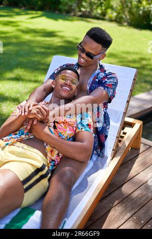 Joyeux jeune gay couple masculin en cuddling, se détendre sur une chaise longue Banque D'Images