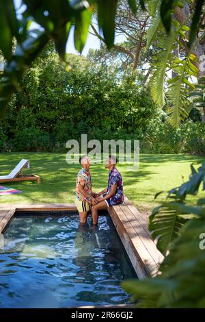 Jeune gay couple de sexe masculin se détendant à la piscine dans l'arrière-cour d'été Banque D'Images