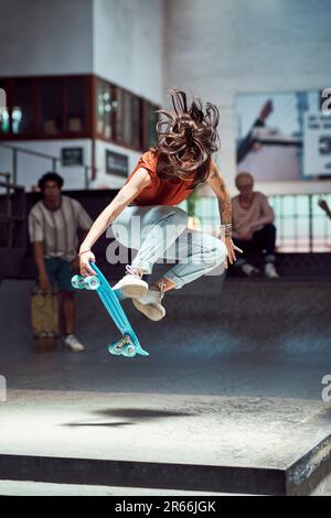 Jeune femme faisant une cascade de skateboard au parc de skateboard Banque D'Images