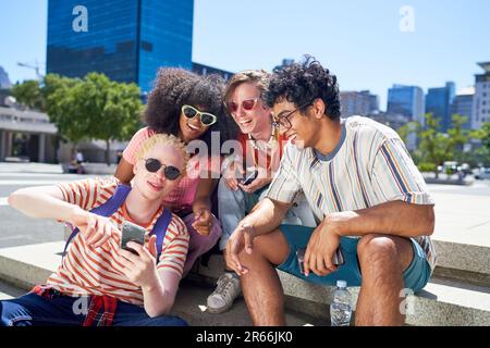 Jeunes amis utilisant un smartphone dans un parc urbain ensoleillé Banque D'Images
