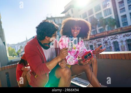 De jeunes amis heureux écoutant de la musique sur un balcon urbain ensoleillé Banque D'Images