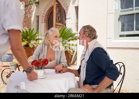 Un serveur sert du café à un couple de personnes âgées heureux à la table du café-terrasse Banque D'Images