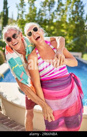 Portrait heureux, joueur couple senior qui s'embrasse au bord de la piscine ensoleillée Banque D'Images