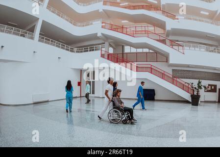 L'atmosphère de la vie hospitalière. Médecins, avec un patient en fauteuil roulant dans le couloir d'un hôpital moderne Banque D'Images