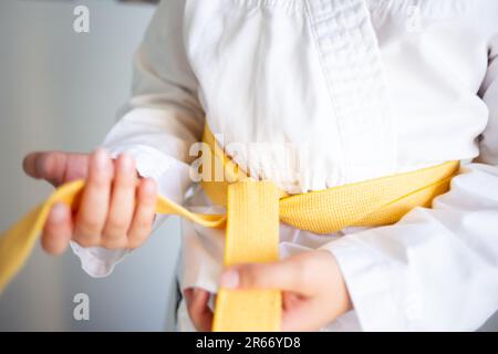 les mains nouent une ceinture jaune en judo, la mise au point douce des détails flous, le sport pour enfants et l'éducation physique Banque D'Images