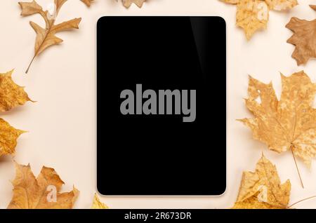 Tablette avec écran vierge sur une table entourée de feuilles d'automne nature, maquette parfaite Banque D'Images