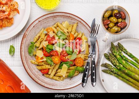 Une délicieuse assiette de pâtes italiennes ornée de tomates fraîches et de feuilles de basilic aromatiques. Pose à plat Banque D'Images