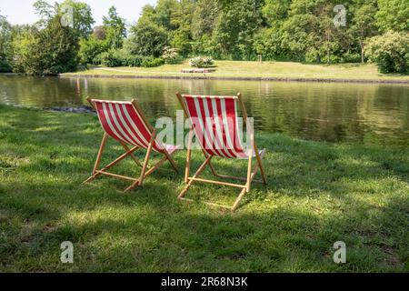 Chaises longues rayées rouges et blanches sur la pelouse sur la rive naturelle d'une rivière, une belle invitation à une journée ensoleillée d'été, espace copie, sélection de foc Banque D'Images