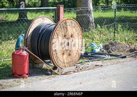 Grande bobine en bois avec câble d'alimentation noir spiralé pour les connexions de maison sur une route de campagne, concept pour l'énergie et l'électricité, focus sélectionné Banque D'Images