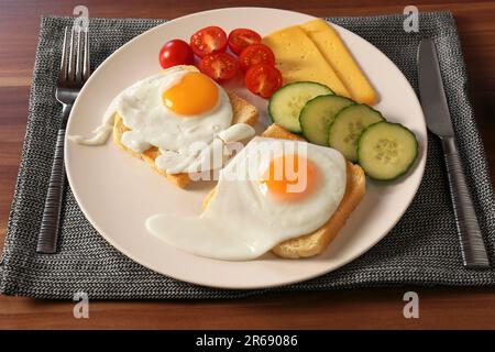 Toasts savoureux avec œufs frits, fromage et légumes sur une table en bois Banque D'Images