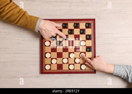 Homme senior jouant aux dames avec une femme à une table en bois blanc, vue de dessus Banque D'Images