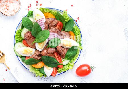 Salade Périgord avec foie de poulet rôti, tomates rouges, concombres, œufs durs, laitue et épinards. Arrière-plan de la table de cuisine noire, vue du dessus Banque D'Images