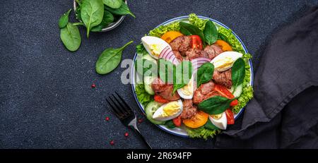 Salade Périgord avec foie de poulet rôti, tomates rouges, concombres, œufs durs, laitue et épinards. Arrière-plan de la table de cuisine noire, vue du dessus Banque D'Images