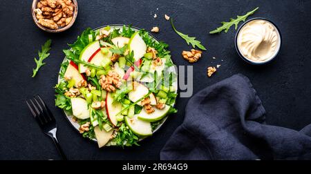 Salade Waldorf aux pommes rouges et vertes, céleri cru, laitue, arugula et noix avec sauce mayonnaise, fond de table noir, vue du dessus Banque D'Images