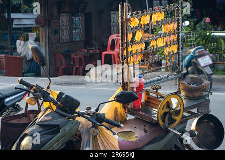 Le calamar pressé séché est suspendu à un support monté sur la moto d'un vendeur de rue à la lumière du coucher du soleil, en Thaïlande Banque D'Images