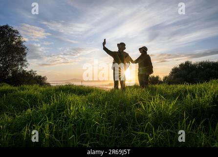 Couple prenant une photo de selfie avec un smartphone au sommet de Mt Eden au lever du soleil. Rangitoto Island au loin. Auckland. Banque D'Images