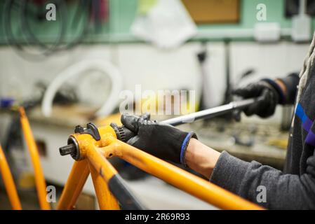 Entretien d'un vélo: Inconnu homme utilisant des gants de protection pour démonter un vélo orange dans son atelier de réparation. Banque D'Images