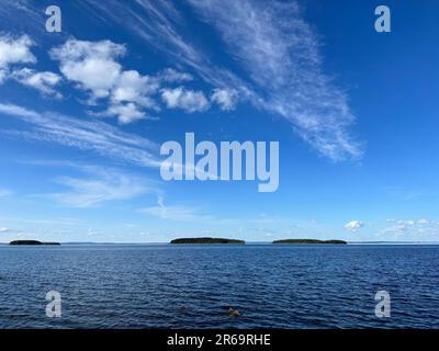 Trois petites îles parsèment un vaste lac bleu sous un ciel lumineux et rempli de nuages. Banque D'Images