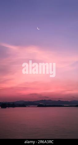 Image verticale, croissant de lune dans un ciel aux couleurs vives et spectaculaire avec paysage de silhouette de montagnes et de lac, crépuscule, fond d'écran de la nature Banque D'Images