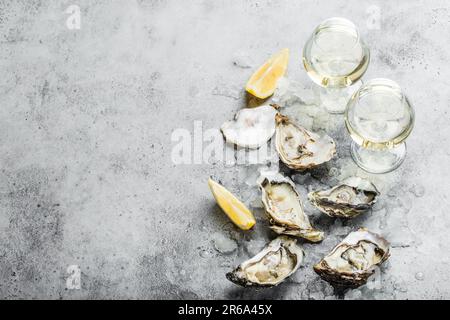 Gros plan d'une demi-douzaine d'huîtres fraîches ouvertes et de coquillages avec des quartiers de citron, deux verres de vin blanc ou de champagne, vue de dessus, béton rustique gris Banque D'Images