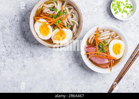 Bols avec ramen de soupe japonais, baguettes, fond rustique en béton blanc. Soupe asiatique traditionnelle avec nouilles, viande, bouillon, œufs. Cuisine asiatique. Banque D'Images