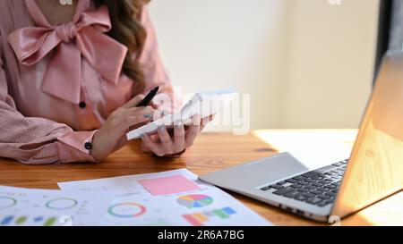 Image rognée d'une belle femme d'affaires asiatique ou comptable dans une robe rose analysant les données financières, à l'aide d'une calculatrice, et travaillant sur un compte Banque D'Images