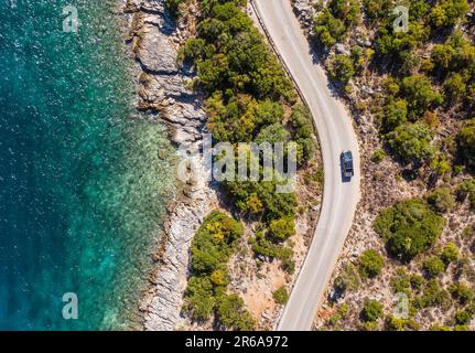 Prise de vue verticale aérienne d'un pick-up se déplaçant par la route courbe près des vagues tranquilles de la mer sur la côte de l'île grecque de Céphalonie. Transport, voyages Banque D'Images