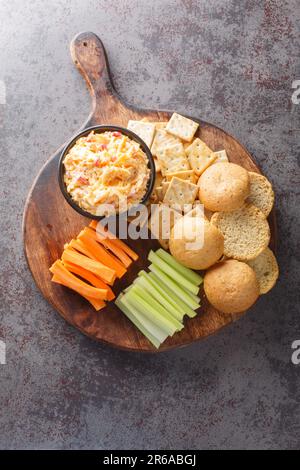 Tartiner au fromage Pimento maison avec des craquelins et des légumes sur le panneau en bois de la table. Vue verticale du dessus Banque D'Images